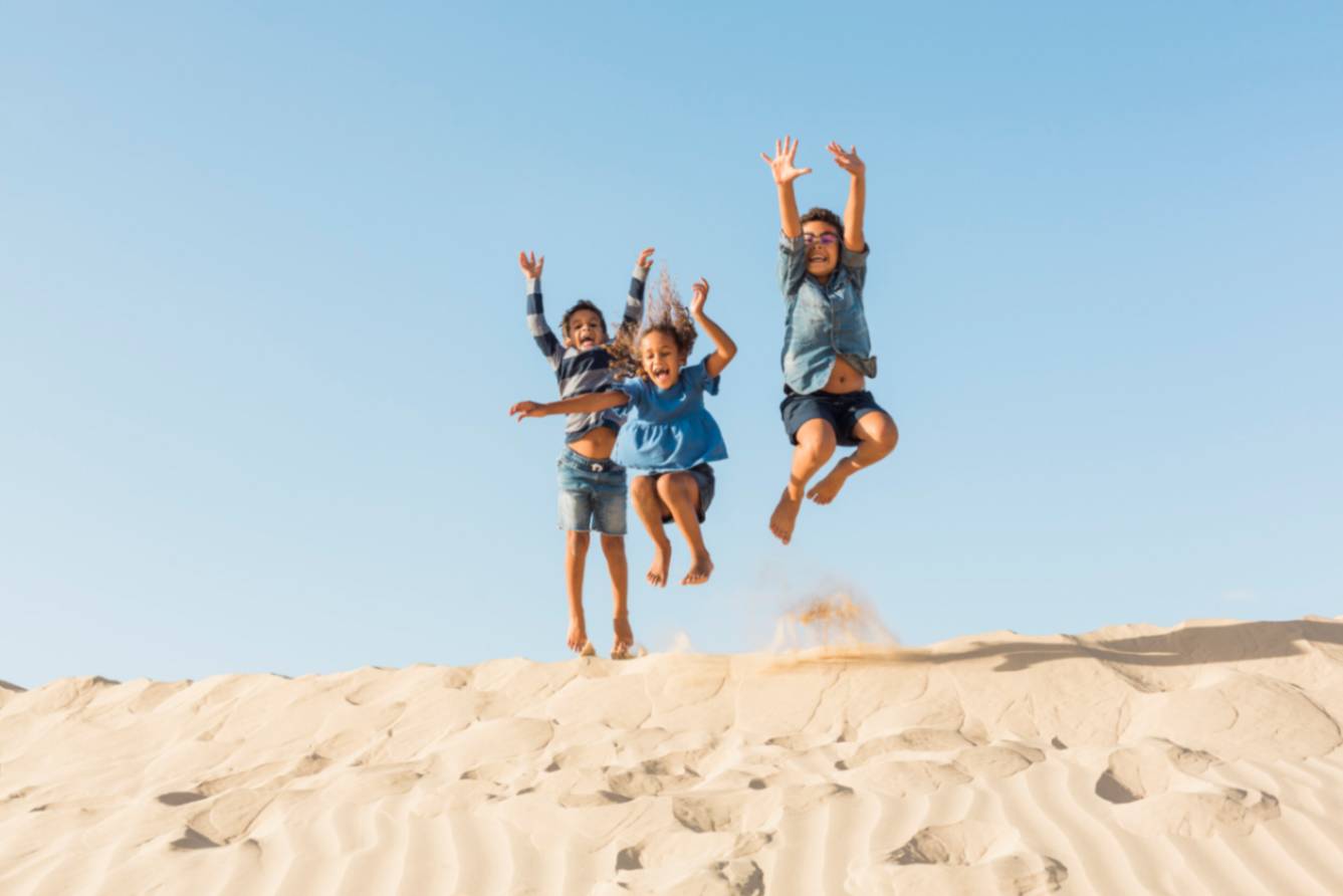 Three happy kids jumping up on sandy surface